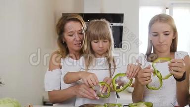 妈妈教两个孩子女儿在厨房的餐桌上做饭，在家里的厨房里用生绿的辣椒。 母亲